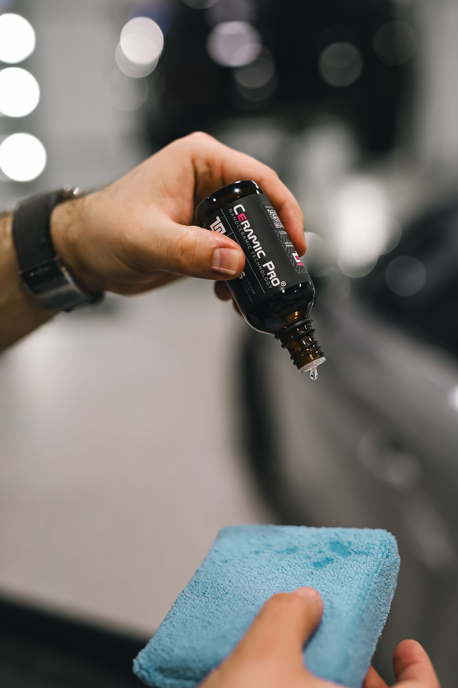 Hands applying a ceramic coating to a car with a blue applicator sponge.