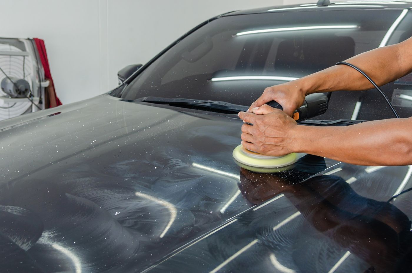 A detailer polishing the dark paintwork of a car.