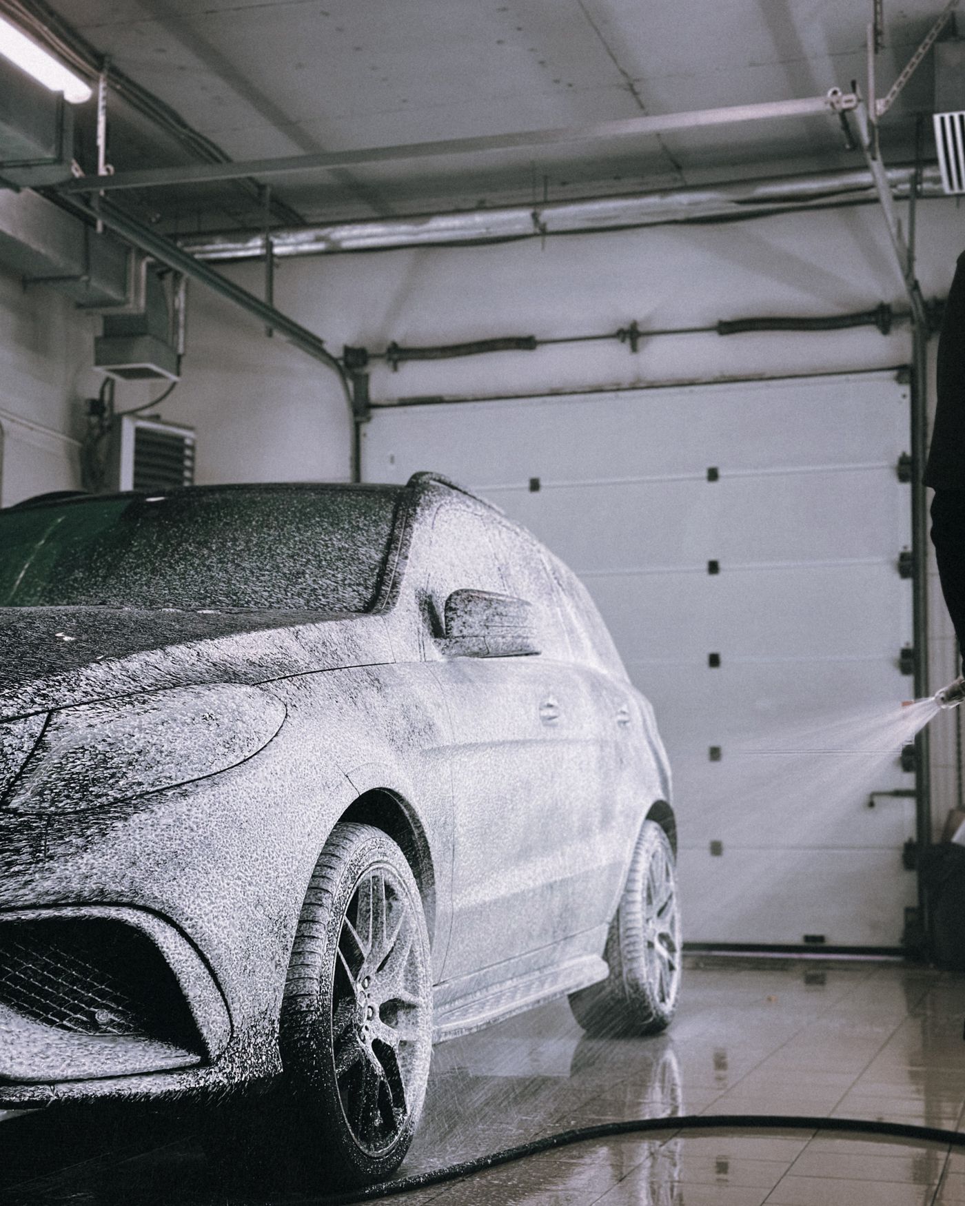 A luxury car covered in wash foam inside a modern garage.