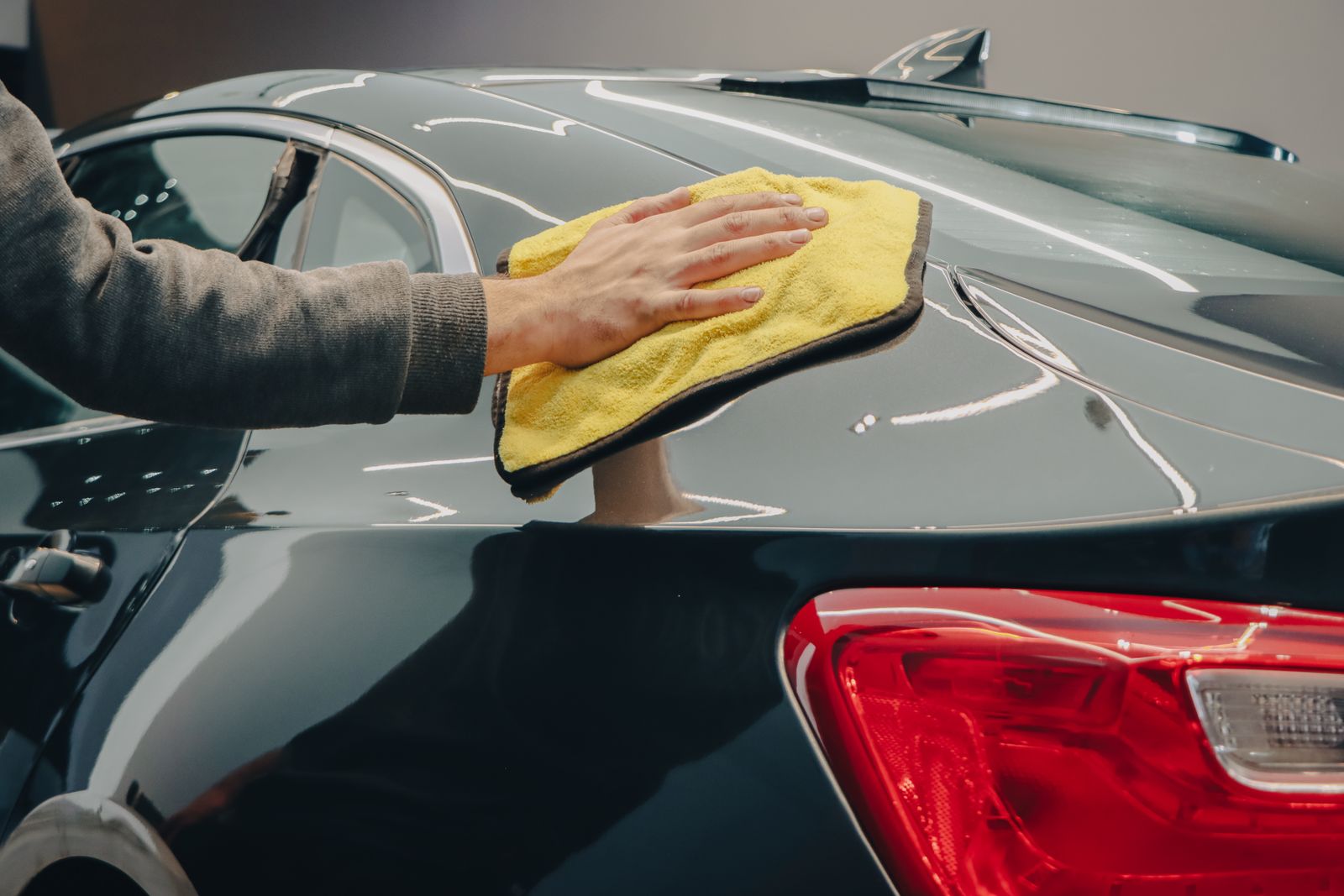 A hand polishing a dark car panel with a cloth during detailing.